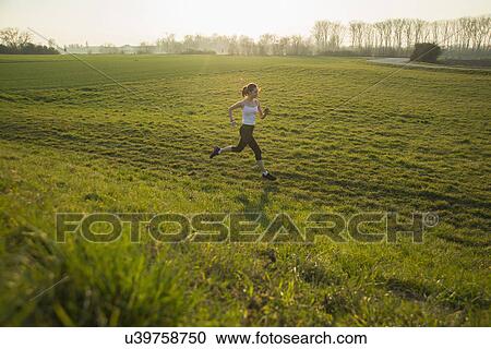 Stock Image - Young female runner in hilly field. Fotosearch