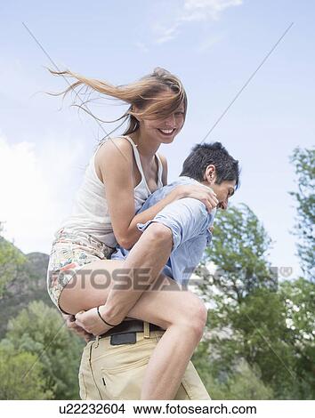 Picture - Young man giving girlfriend piggy back ride. Fotosearch