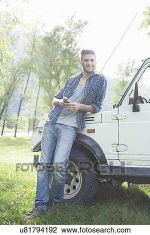Stock Image - Young man leaning against off road vehicle. Fotosearch