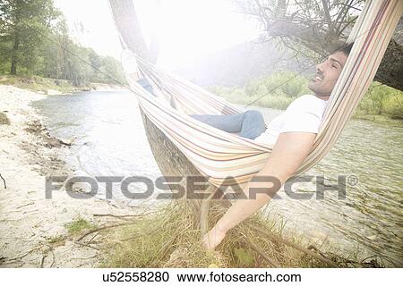 Young man lounging in hammock on Toce riverbank, Piemonte, Italy View Large Photo Image Stock Image - Young man lounging in hammock on Toce riverbank, Piemonte, Italy. Fotosearch