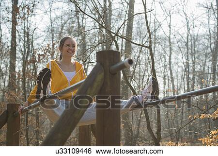 Stock Photograph - Young woman balancing on parallel bars on forest assault course. Fotosearch