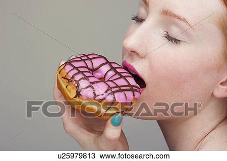 Stock Image - Young woman biting donut. Fotosearch