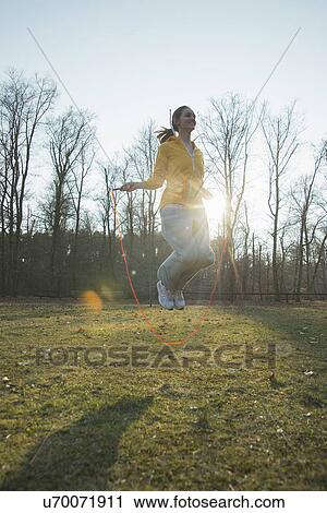 Stock Image - Young woman exercising in field with skipping ropes. Fotosearch