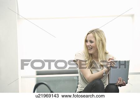 Stock Image - Young woman holding digital tablet laughing. Fotosearch