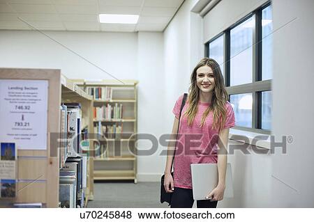 Stock Photo - Young woman holding laptop in library. Fotosearch