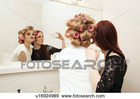 Stock Photo - Young woman in curlers and friend taking selfie. Fotosearch