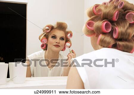Stock Image - Young woman in curlers putting on make-up. Fotosearch