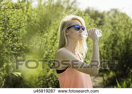 Stock Photo - Young woman in park drinking bottle of water. Fotosearch