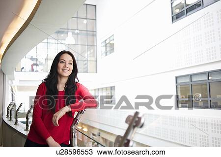 Stock Image - Young woman leaning on railing, portrait. Fotosearch