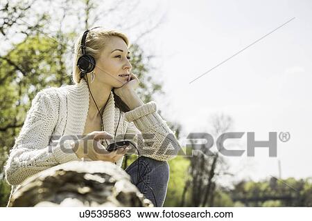Stock Image - Young woman listening to headphones in forest. Fotosearch
