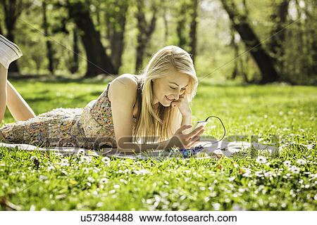 Young woman lying in forest looking at smartphone View Large Photo Image Stock Photo - Young woman lying in forest looking at smartphone. Fotosearch