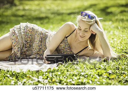 Stock Photography - Young woman lying in forest looking at digital tablet. Fotosearch
