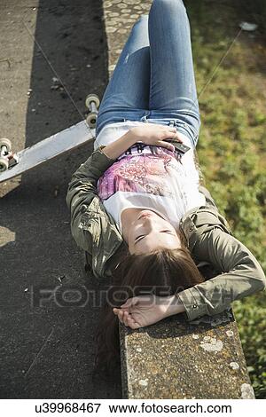 Stock Photo - Young woman lying on wall asleep. Fotosearch