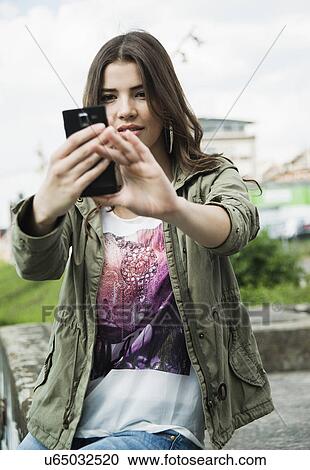 Stock Image - Young woman photographing herself with smartphone. Fotosearch