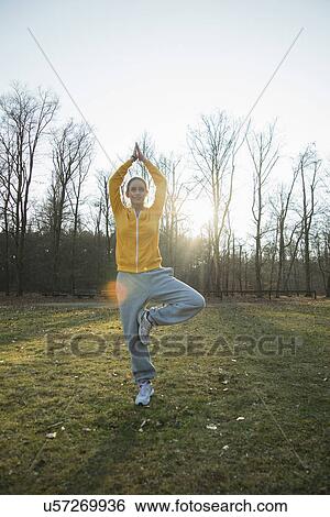 Stock Photograph - Young woman practicing yoga in field. Fotosearch