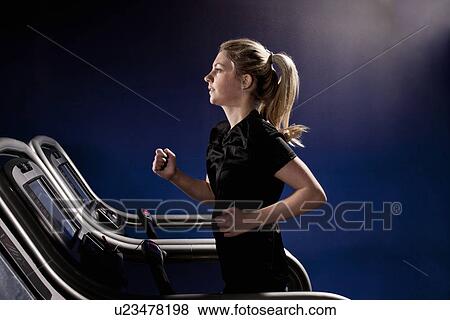 Stock Photo - Young woman running on treadmill at gym in altitude centre. Fotosearch