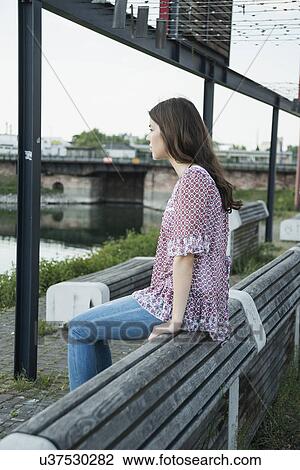 Young woman sitting on bench View Large Photo Image Stock Image - Young woman sitting on bench. Fotosearch