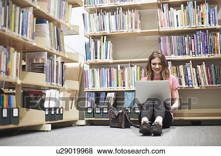 Young woman sitting on floor in library using laptop View Large Photo Image Stock Photo - Young woman sitting on floor in library using laptop. Fotosearch
