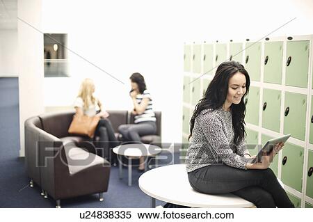 Stock Photography - Young woman sitting on table using digital tablet. Fotosearch