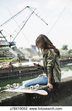 Young woman sitting on wall using cell phone View Large Photo Image Stock Image - Young woman sitting on wall using cell phone. Fotosearch