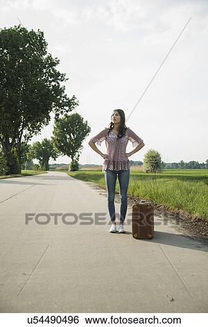 Young woman standing on country road with suitcase View Large Photo Image Stock Photograph - Young woman standing on country road with suitcase. Fotosearch