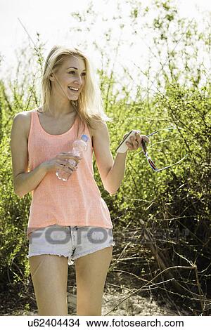 Young woman strolling in park with water bottle and smartphone View Large Photo Image Picture - Young woman strolling in park with water bottle and smartphone. Fotosearch