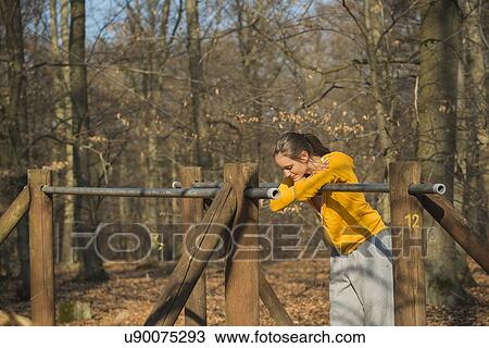 Stock Image - Young woman taking a break on forest assault course. Fotosearch