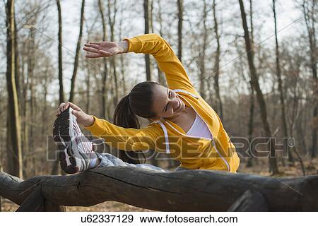 Stock Photo - Young woman touching toes on assault course in forest. Fotosearch