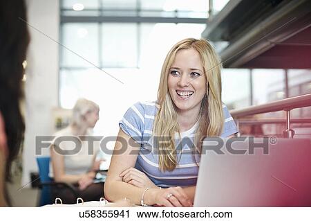 Stock Image - Young woman using laptop in library. Fotosearch