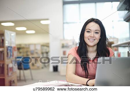 Stock Image - Young woman using laptop in library. Fotosearch