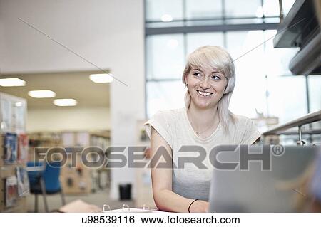 Stock Photograph - Young woman using laptop in library. Fotosearch