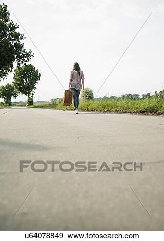 Young woman walking on country road carrying suitcase View Large Photo Image Stock Photo - Young woman walking on country road carrying suitcase. Fotosearch