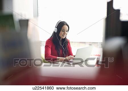 Young woman wearing headphones using laptop View Large Photo Image Stock Image - Young woman wearing headphones using laptop. Fotosearch