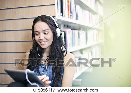 Stock Photo - Young woman wearing headphones using digital tablet. Fotosearch