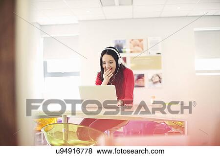 Young woman wearing headphones using laptop View Large Photo Image Stock Photo - Young woman wearing headphones using laptop. Fotosearch