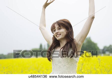 Stock Photograph - Young woman with arms raised in yellow field. Fotosearch