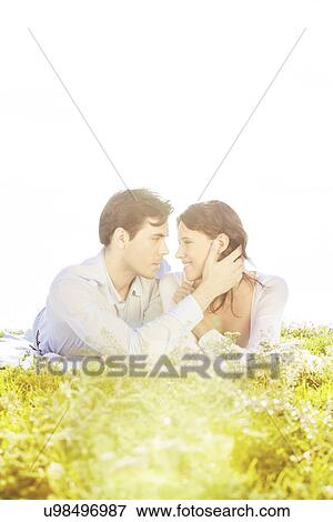 Affectionate man touching woman while looking at her on grass against clear sky View Large Photo Image Stock Photo - Affectionate man touching woman while looking at her on grass against clear sky. Fotosearch