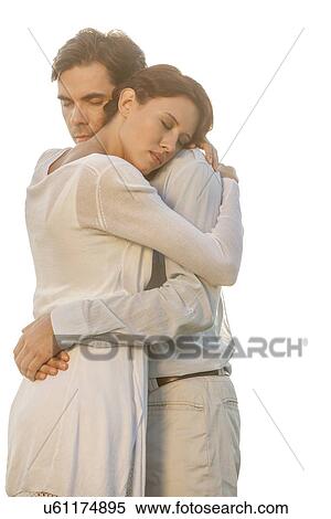 Stock Photography - Affectionate young couple with eyes closed hugging in park against clear sky. Fotosearch