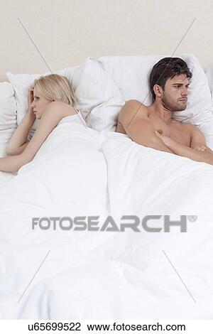 Stock Image - Angry young couple avoiding each other in bed. Fotosearch