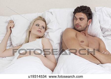 Picture - Angry young couple looking at each other in bed. Fotosearch
