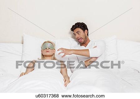 Stock Photo - Angry young man teasing sleeping woman in bed. Fotosearch