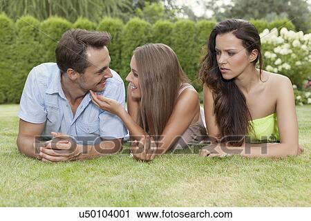 Stock Image - Angry young woman looking at loving couple at park. Fotosearch