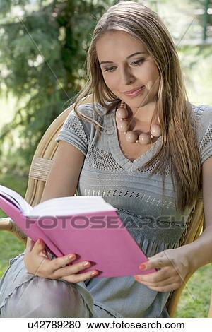 Stock Image - Attractive young woman reading book in park. Fotosearch