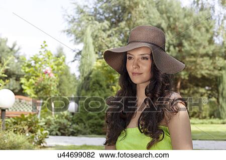 Stock Image - Attractive young woman wearing sunhat in park. Fotosearch