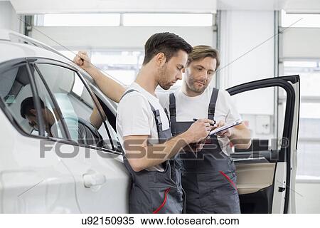 Automobile mechanics checking checklist while standing by car in workshop View Large Photo Image Stock Photography - Automobile mechanics checking checklist while standing by car in workshop. Fotosearch