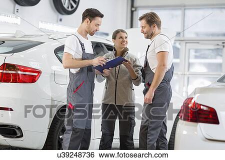 Stock Photograph - Automobile mechanics discussing over clipboard in car repair shop. Fotosearch
