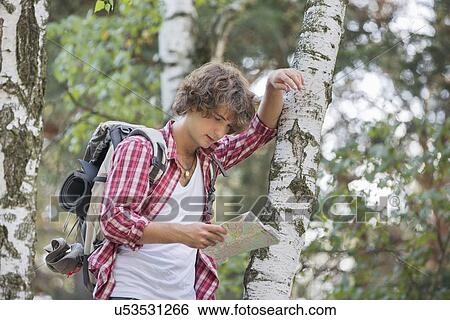 Stock Photograph - Backpacker reading map while leaning on tree trunk in forest. Fotosearch