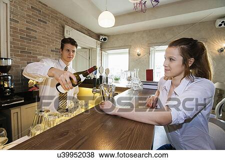 Bartender pouring wine for female customer at restaurant counter View Large Photo Image Stock Photo - Bartender pouring wine for female customer at restaurant counter. Fotosearch