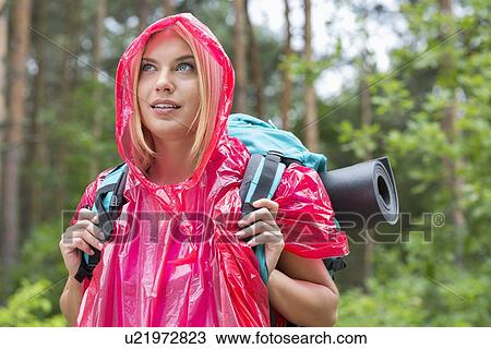 Stock Image - Beautiful backpacker in raincoat looking away at forest. Fotosearch