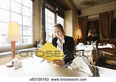 Stock Image - Beautiful customer reading menu at restaurant table. Fotosearch